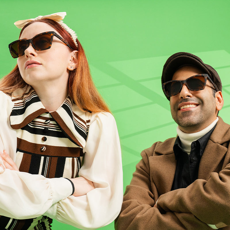 A man and woman in stylish brown outfits pose wearing brown tortoiseshell angled cat-eye sunglasses with brown lenses.